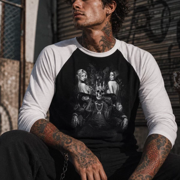 Man wearing a white and black raglan shirt featuring a graphic of a crowned skull on a throne with two women